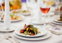 Formally set table with a beef and vegetable dinner plate and filled wine glass